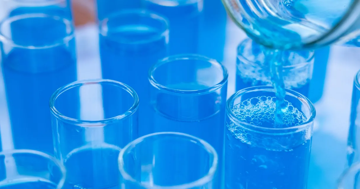 Recipientes de vidro de laboratório recebendo líquido azul, ambiente que usa água desmineralizada