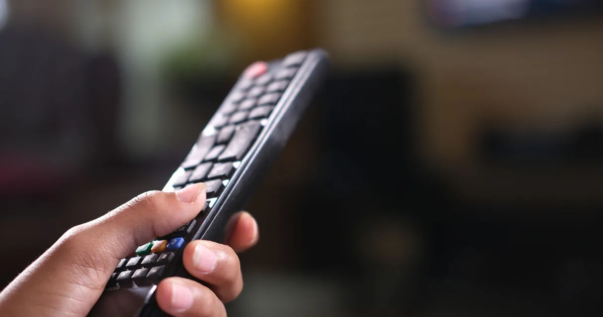 Mão segurando controle remoto de televisão, ilustrando a comparação do melhor IPTV do Brasil